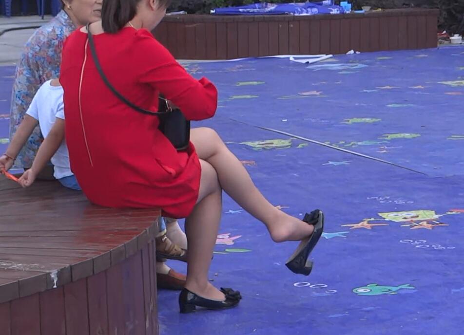 The beautiful woman in a red dress dangling shoeplay when sitting on a chair